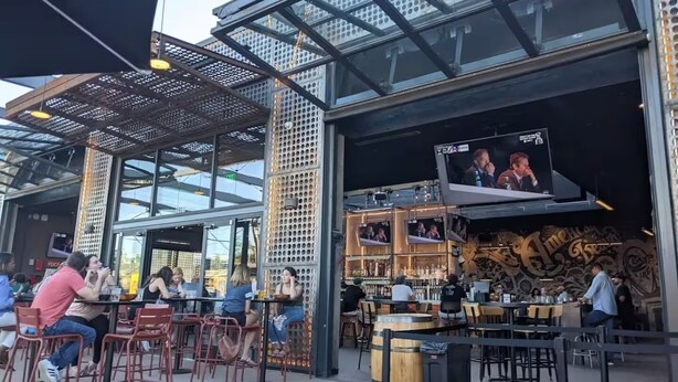 An outdoor seating area with tables and chairs, a bar with multiple screens, and a modern architectural design with glass and metal elements. - Bright and Modern Studio Guesthouse - near RiNo! (Denver)
