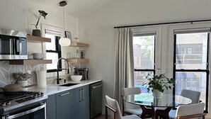 A modern kitchen with a built-in oven, microwave, and coffee maker. There is a dining area with a glass table and chairs, and a view of the city through large windows. - Bright and Modern Studio Guesthouse - near RiNo! (Denver)