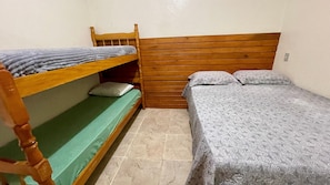 A room with a bunk bed, a single bed, and a wooden headboard.
