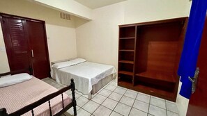 Een kleine, eenvoudige kamer met twee bedden, een kledingkast en een betegelde vloer.