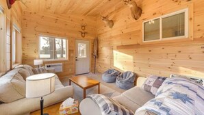 A cozy cabin interior with a wooden ceiling, a sofa, a table, and a window.