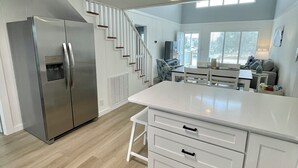 A modern kitchen with a stainless steel refrigerator, white cabinetry, and a wooden floor. - Cozy 5BR-2.5BA Cottage on Canal, Private Heated Pool, Private Boat Dock (Ocean Isle Beach)