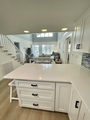 A spacious kitchen with a large island, white cabinetry, and a staircase leading to an upper level.
