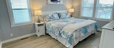 A bedroom with a bed, nightstands, a ceiling fan, and two windows with blinds.