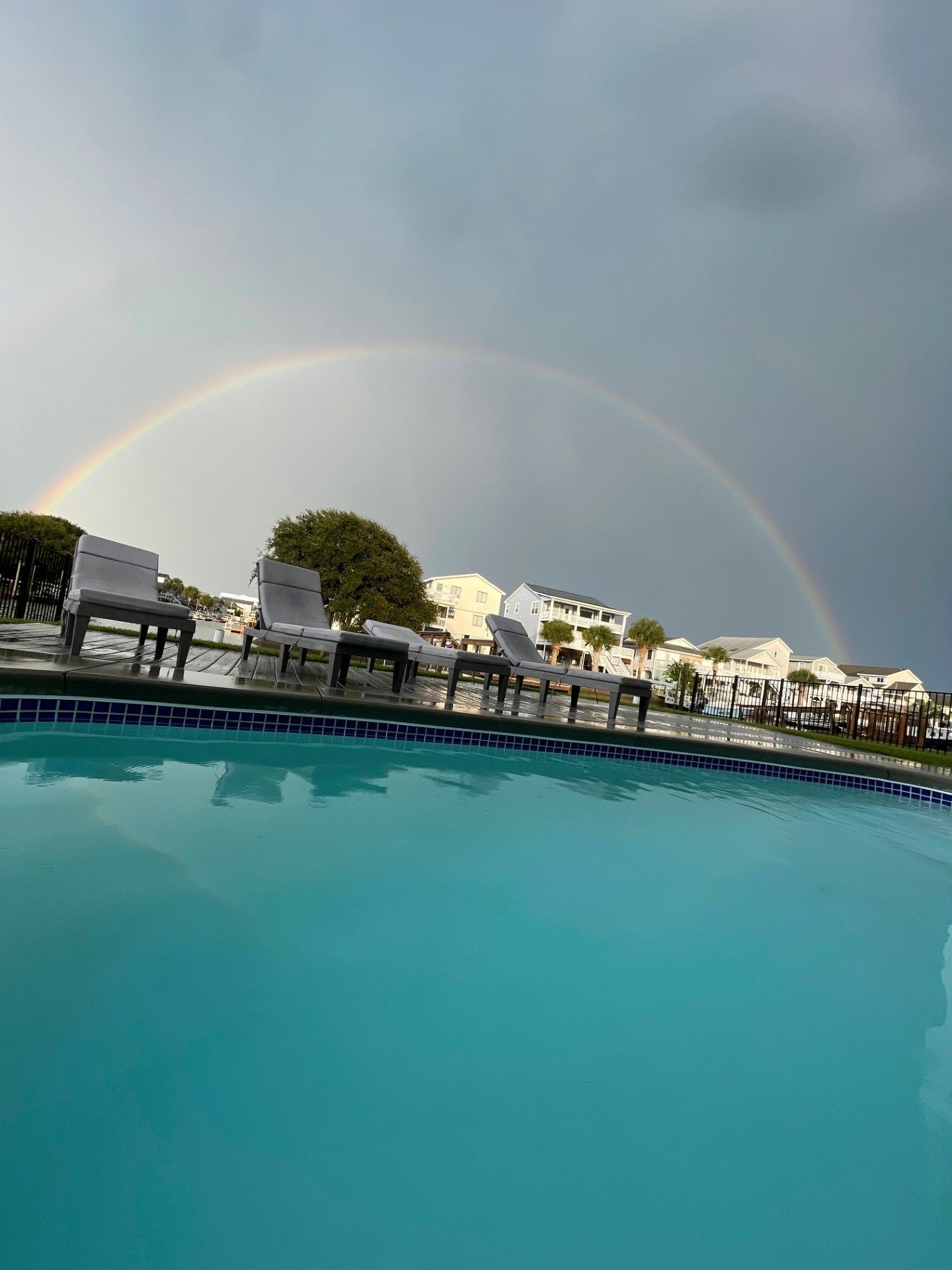 A swimming pool with lounge chairs and a rainbow in the background.