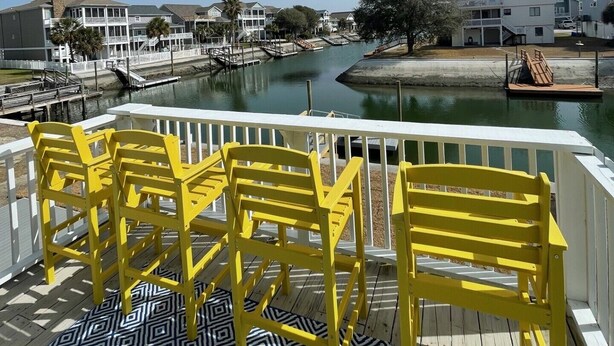 A balcony with yellow chairs overlooking a marina with boats and buildings. - Cozy 5BR-2.5BA Cottage on Canal, Private Heated Pool, Private Boat Dock (Ocean Isle Beach)