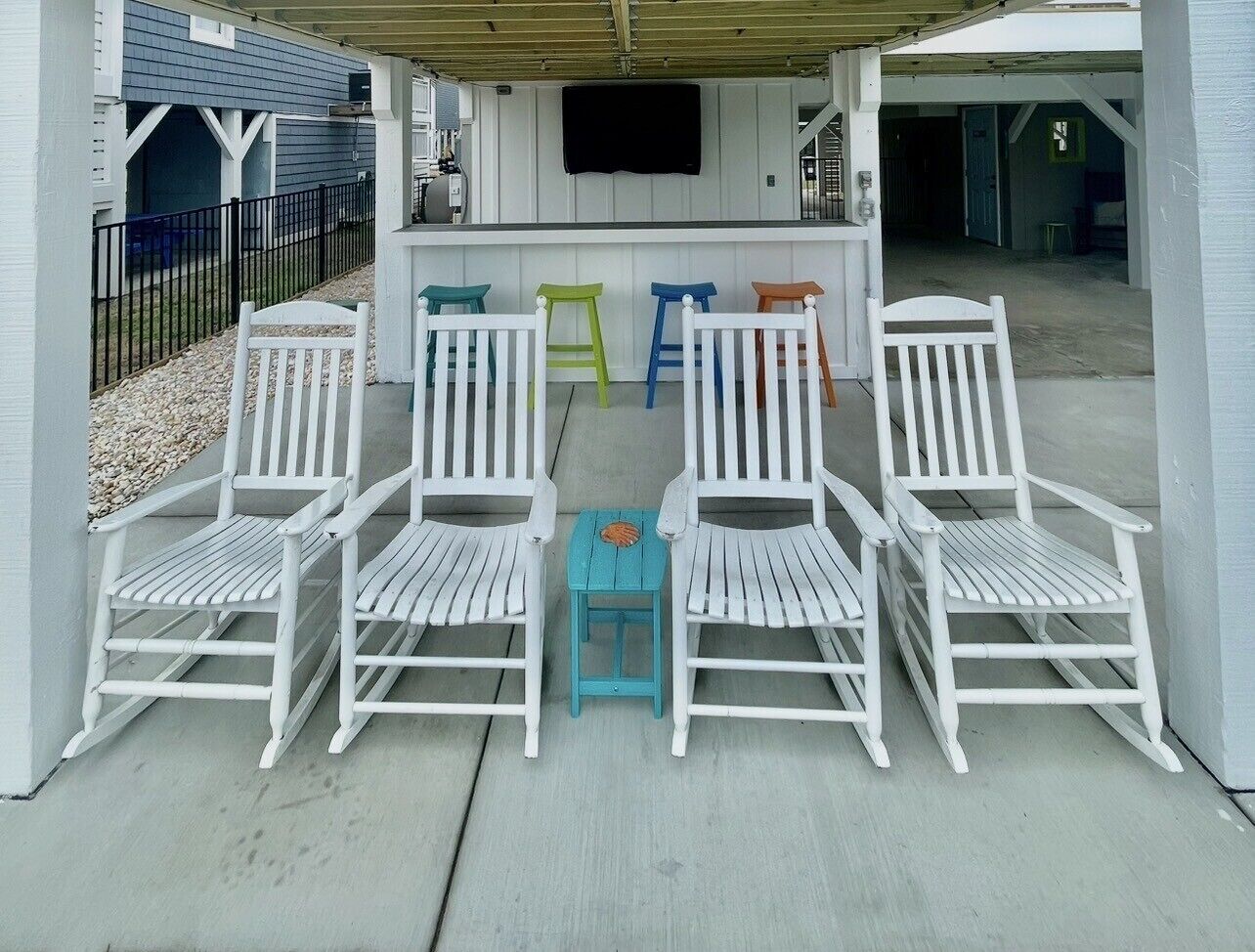 A covered outdoor seating area with white chairs and a small table.
