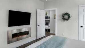 A modern bedroom with a fireplace, a TV mounted on the wall, and a door leading to a closet.