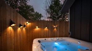 A hot tub with built-in lighting, surrounded by a wooden fence and a dark building.