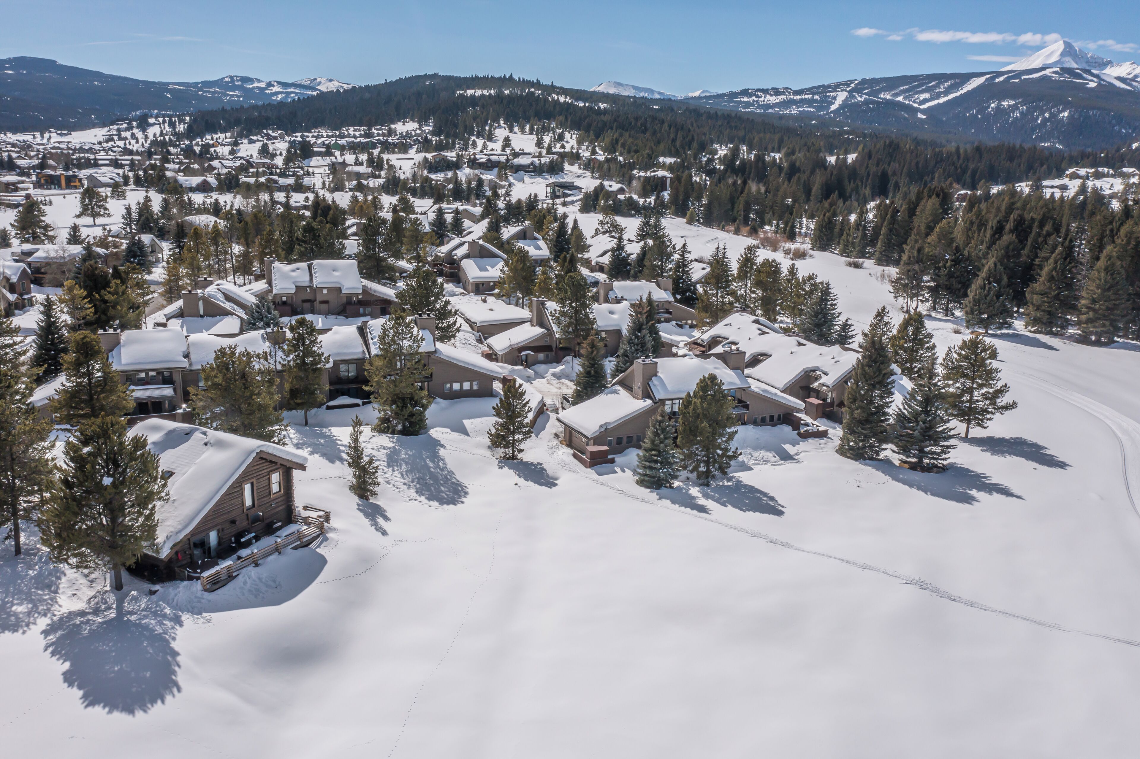 A snow-covered lodge with multiple cabins, surrounded by trees and mountains in the background.