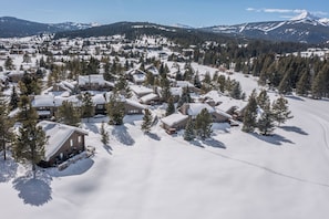 A snow-covered resort with multiple cabins, surrounded by trees and mountains. - Ski, Hike, Soak + Swim | Snowbound Retreat (Big Sky)