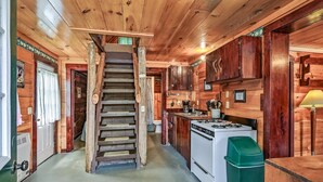 A wooden cabin interior with a central staircase, a kitchen area with a stove and sink, and wooden cabinets. - Charming 3-bedroom cottage in peaceful Solon with WiFi (Solon)