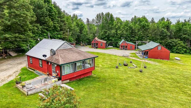 A red house with a large window and a porch, surrounded by a well-maintained lawn and trees. - Charming 3-bedroom cottage in peaceful Solon with WiFi (Solon)