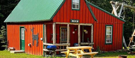 A red wooden building with a green roof, a sign reading "DEER", and a picnic table in front.