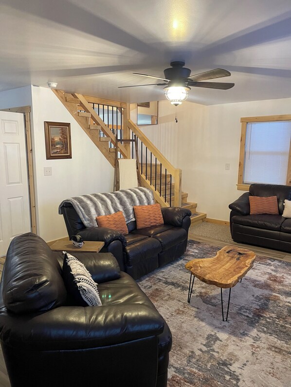 A living room with a black leather sofa, a wooden coffee table, and a staircase with wooden railings.