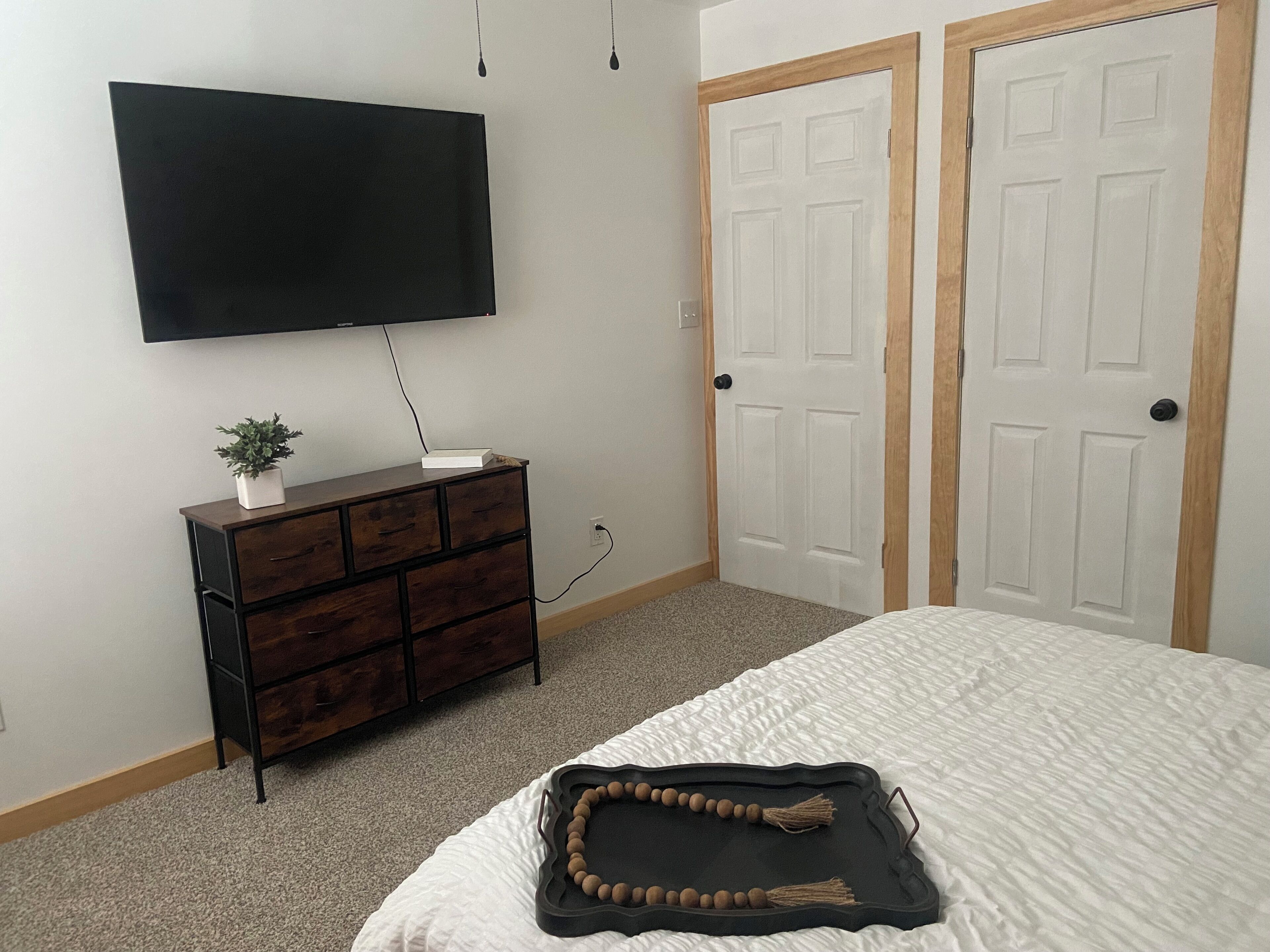 A bedroom with a bed, a dresser, a TV mounted on the wall, and two doors.