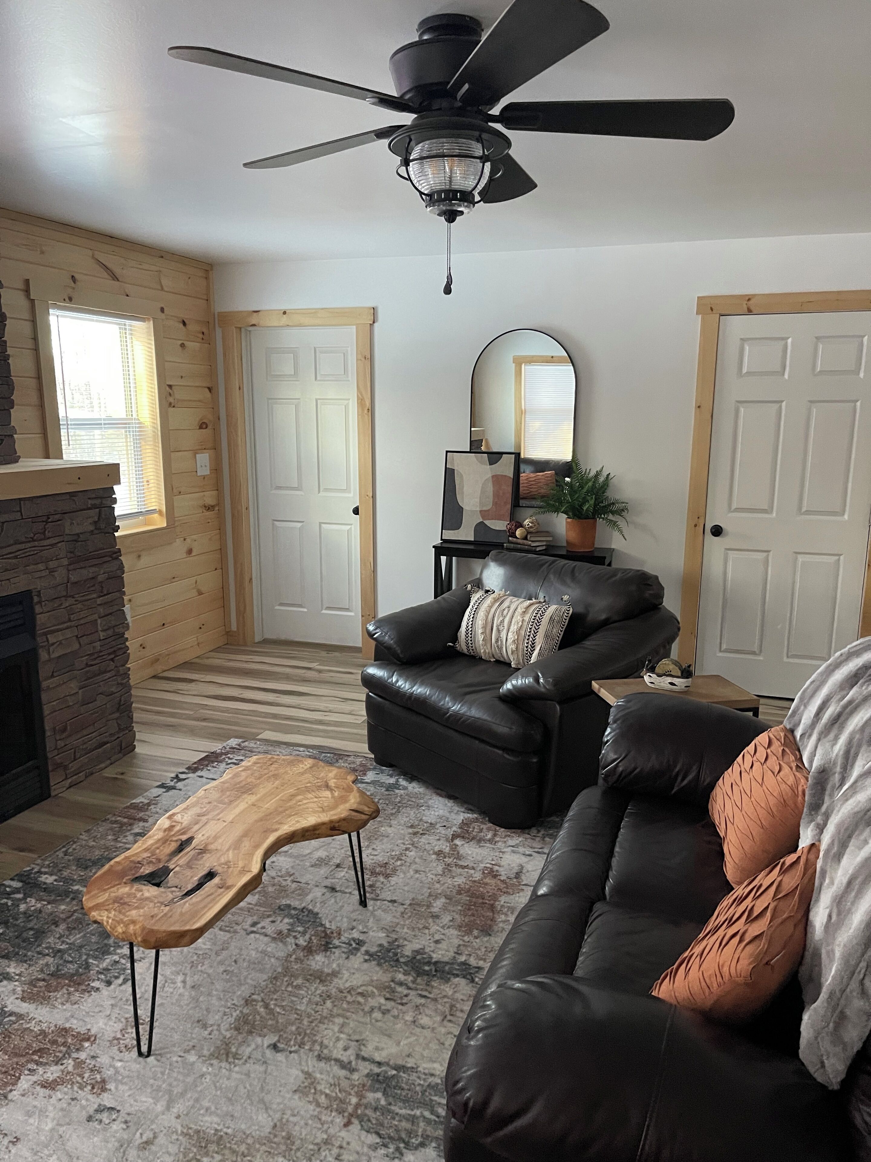 A living room with a fireplace, a leather sofa, a coffee table, and a ceiling fan.