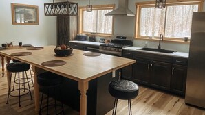 Una cucina moderna con isola centrale, sgabelli da bar, luci a sospensione e ampie finestre.