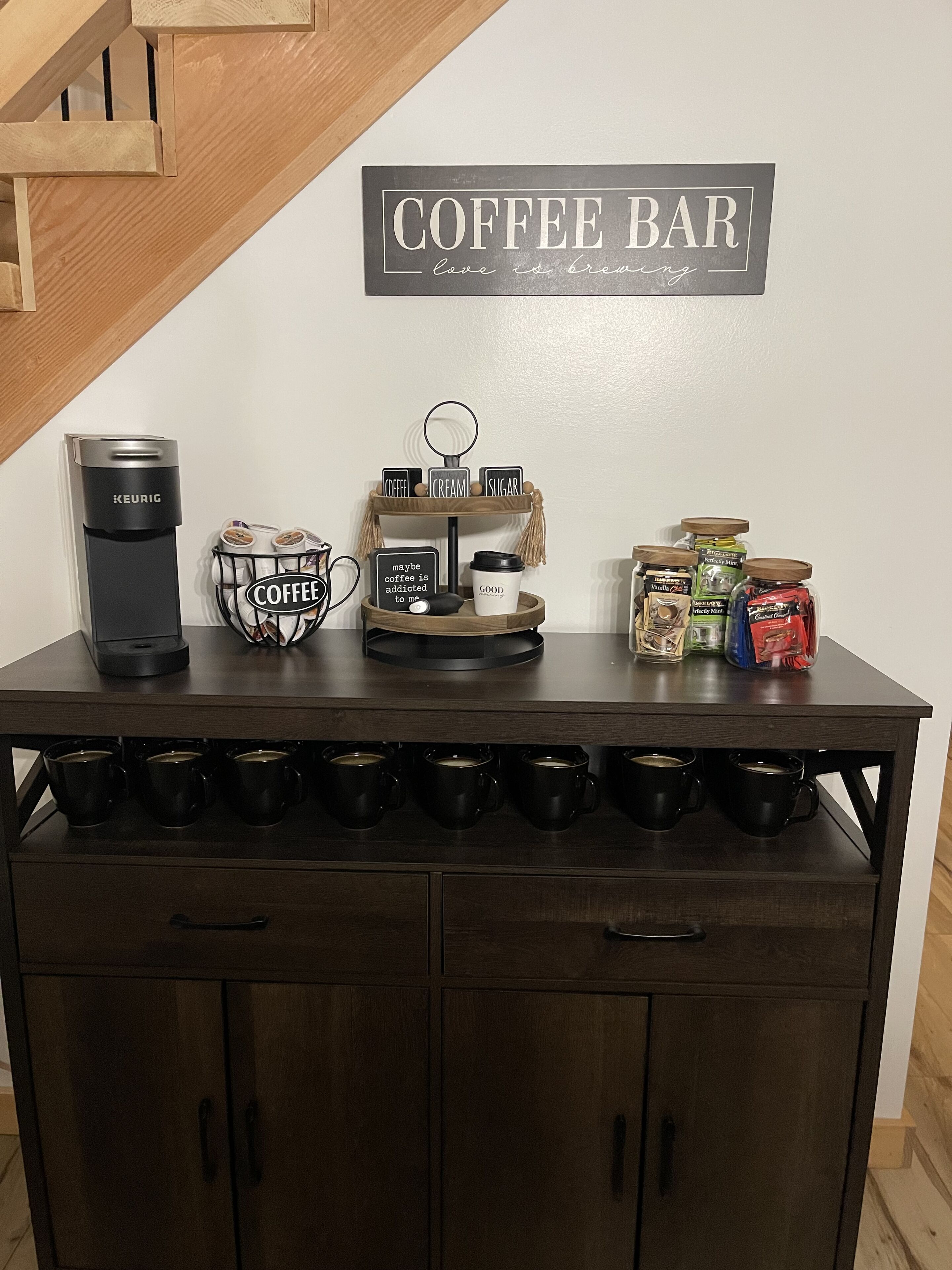 En kaffestation med en Keurig-kaffemaskin, kaffekoppar, ett fat med kaffebönor och en skylt med texten: ”Här bryggs det kärlek i form av kaffe”.