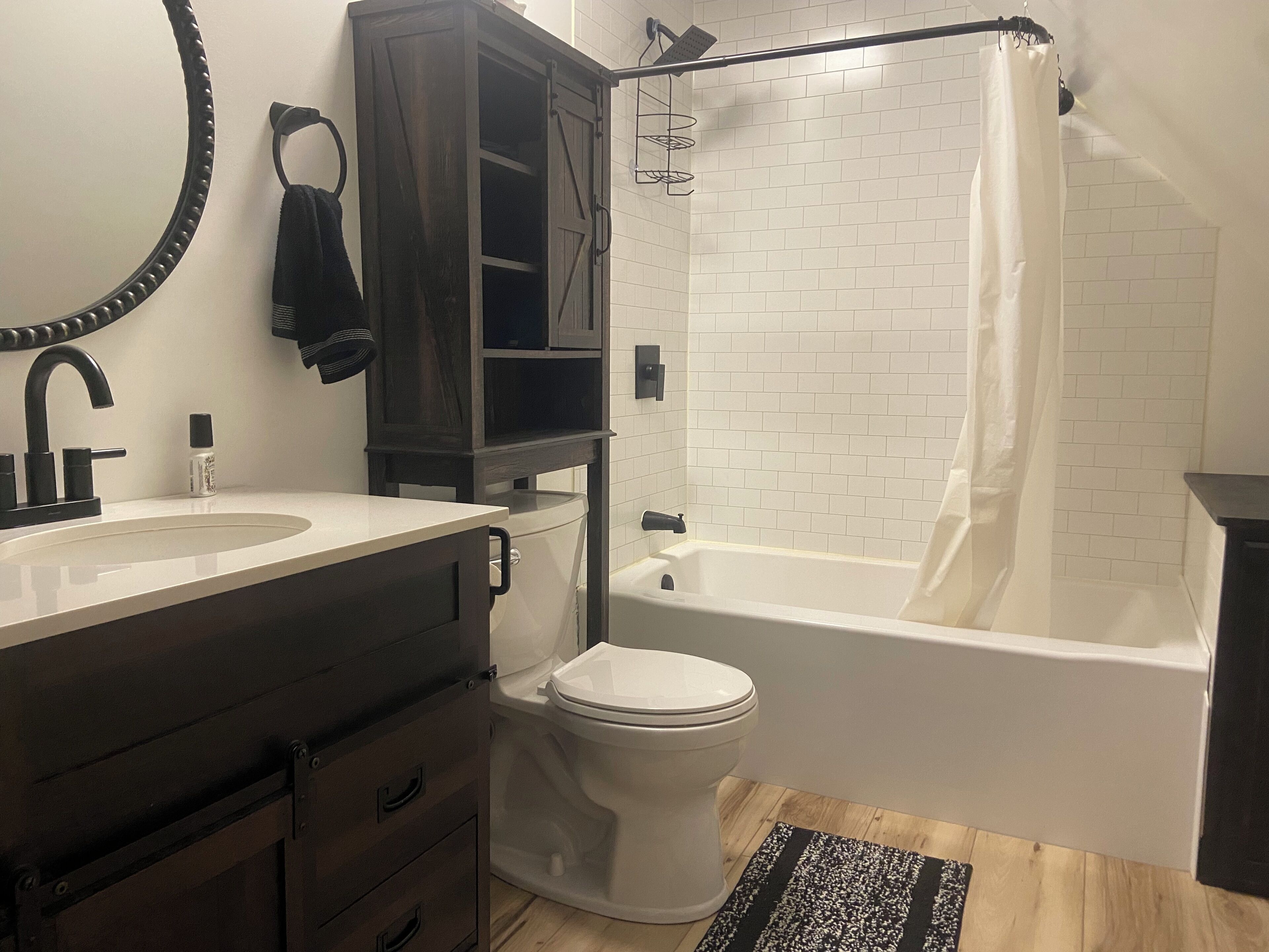 Un baño con lavamanos blanco, mueble de madera oscura, inodoro y bañera blanca con cortina de ducha.