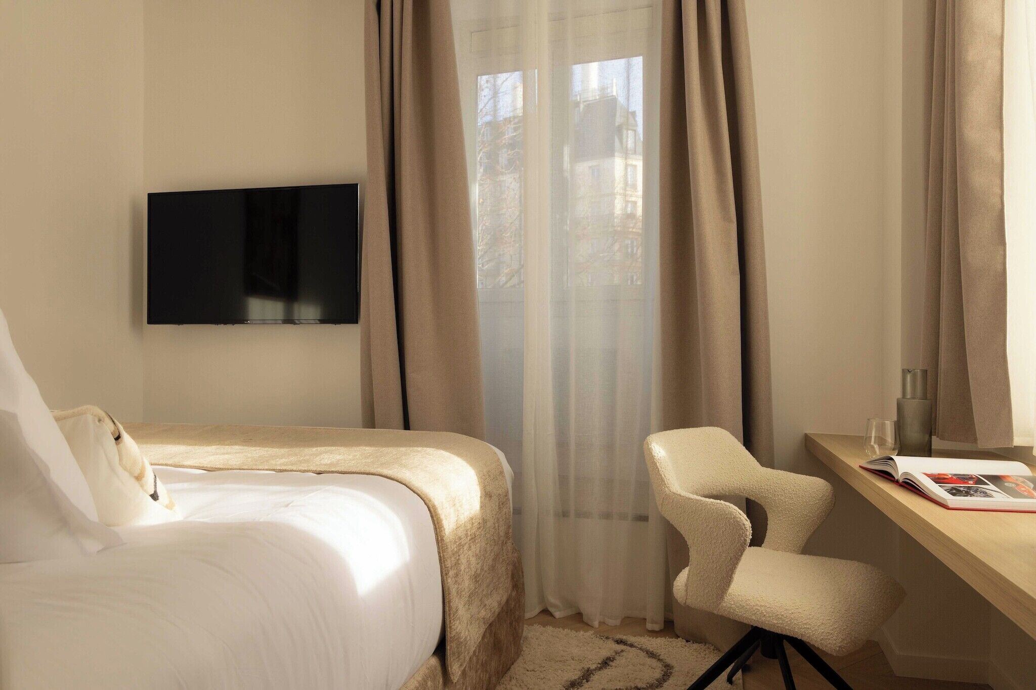 Une chambre d’hôtel avec un lit, un bureau, une chaise, une télévision et une fenêtre avec des rideaux.