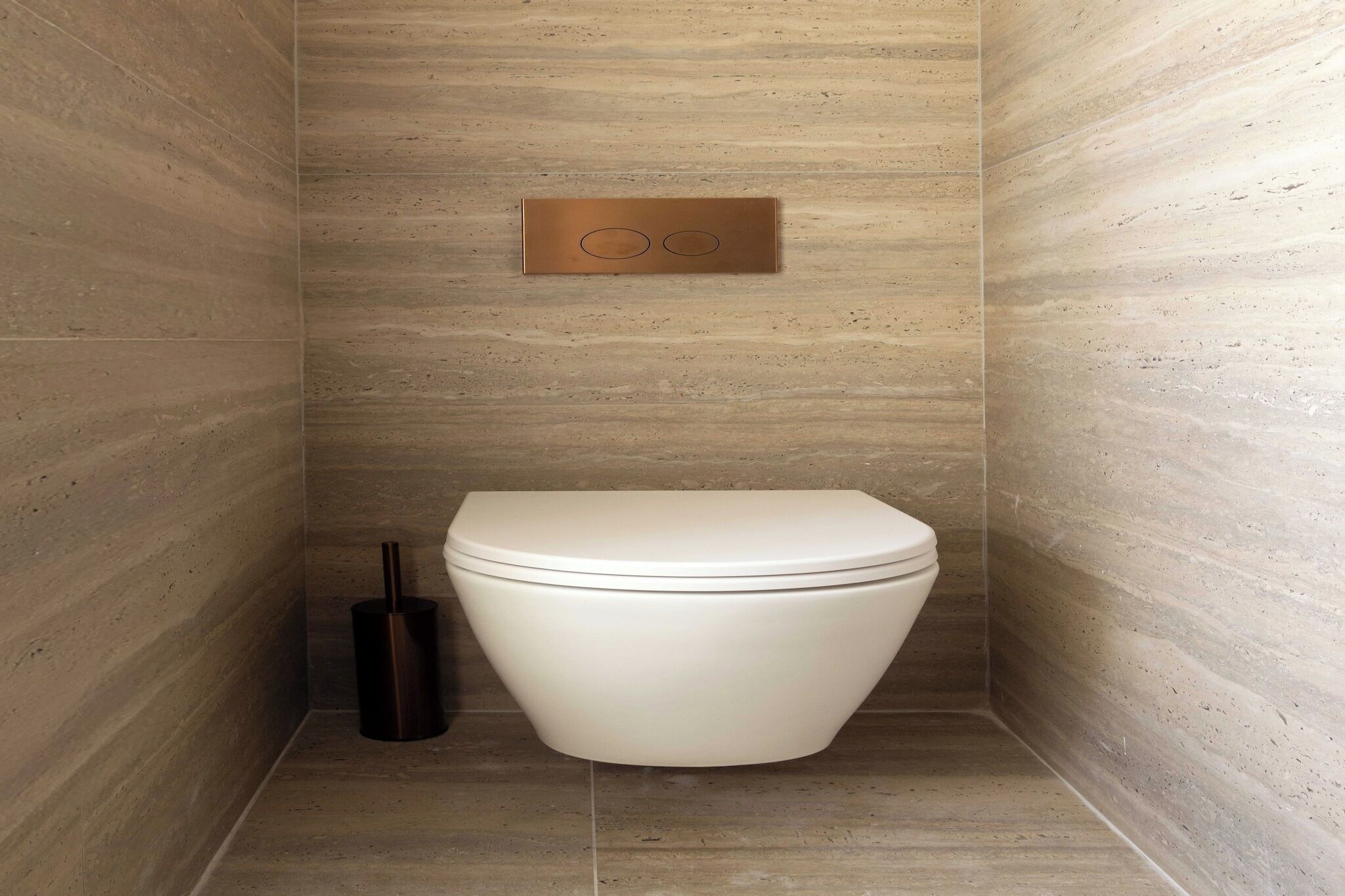 A modern bathroom with a white toilet, a flush handle, and a toilet brush.