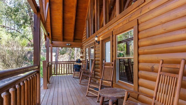 Een houten blokhut met een veranda, voorzien van houten stoelen en een tafel.