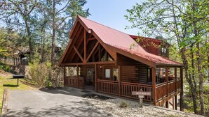 Een vakantiehuisje van hout met een rood dak, een veranda en een bordje met de tekst 'Zijn we er bijna?'.