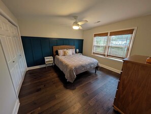 A bedroom with a bed, a nightstand, a dresser, a ceiling fan, and a window.