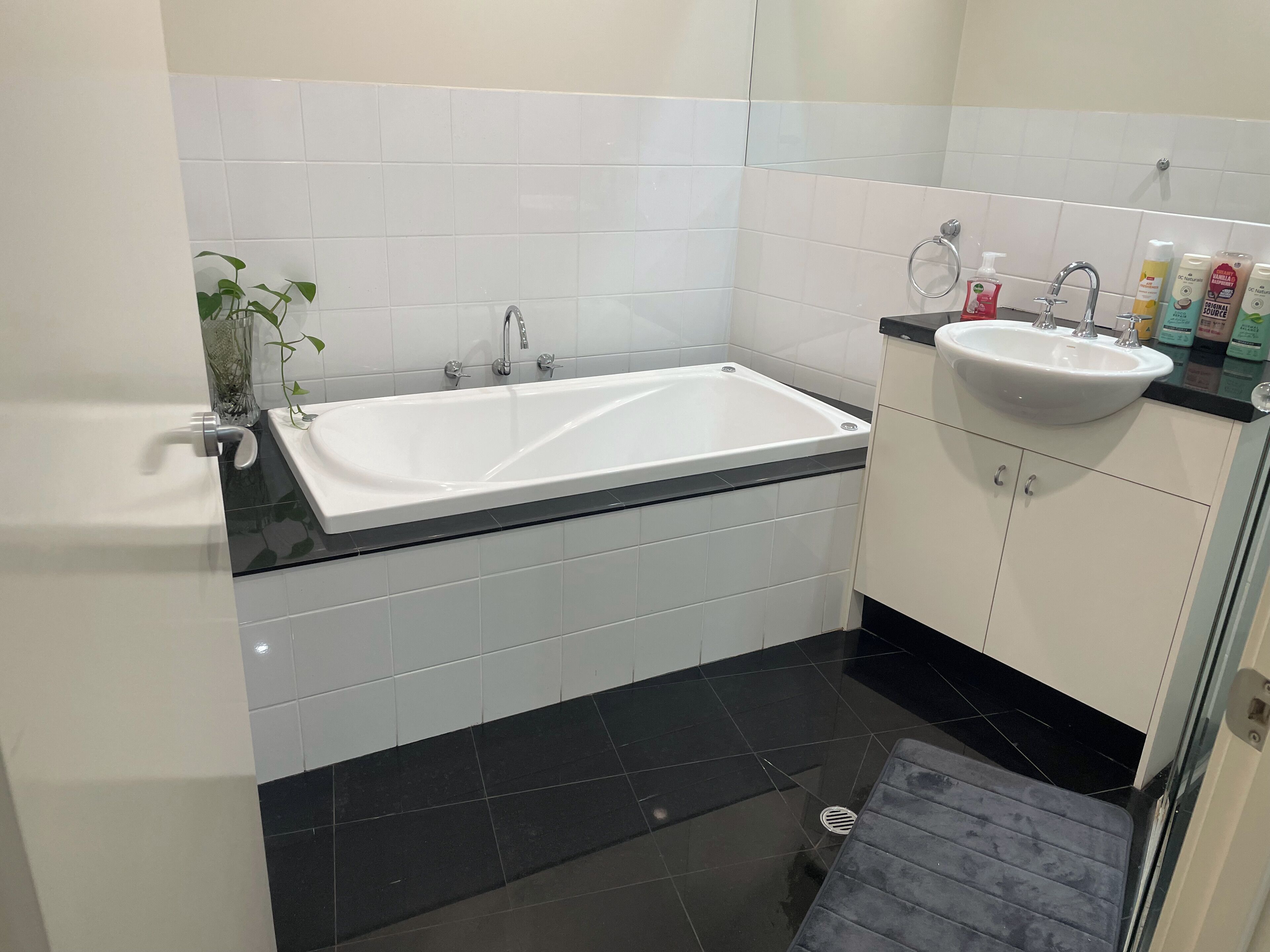 A modern bathroom with a white bathtub, a black sink, and a glass shower enclosure.
