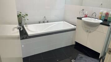 A modern bathroom with a white bathtub, a black sink, and a glass shower enclosure.