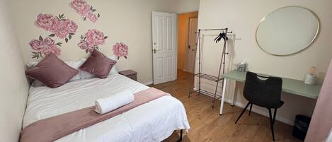 A bedroom with a bed, a desk, a chair, a hanging clothes rack, and a mirror.