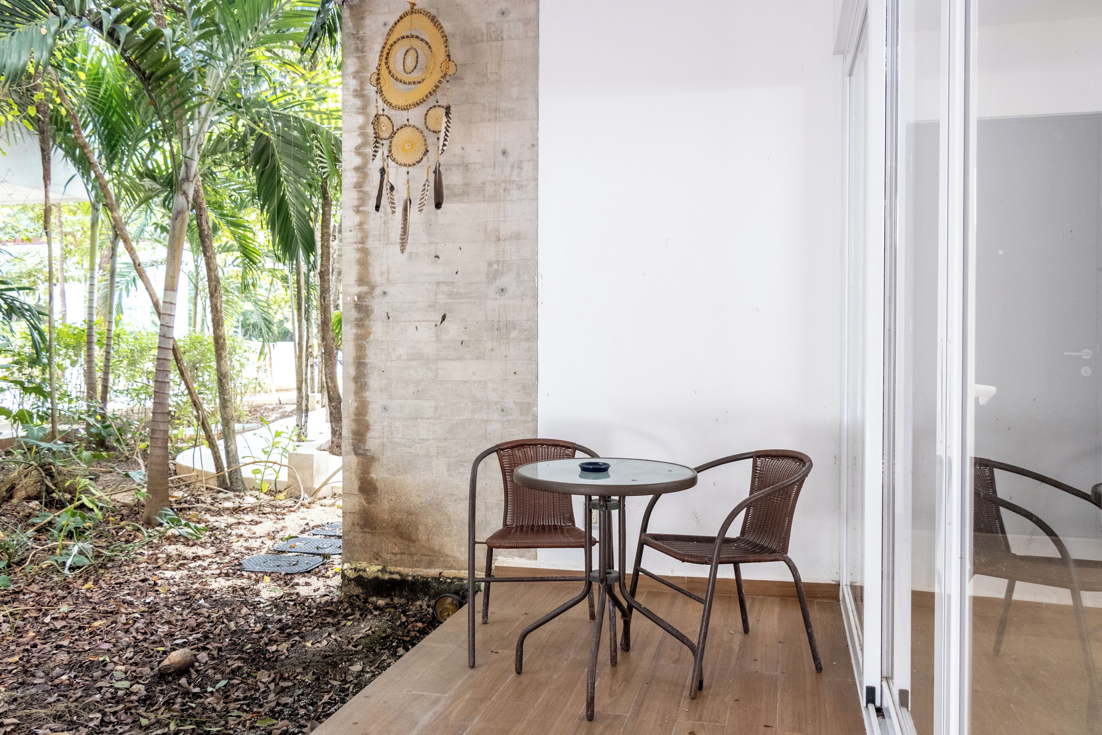 A patio with a round table and two wicker chairs, a concrete wall, and a glass door leading inside.