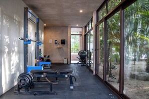 Ein Fitnessstudio mit Gewichthebern, einer Bank und großen Fenstern mit Blick auf einen Garten.