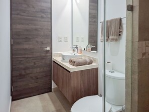 A modern bathroom with a wooden door, a sink with a mirror, and a toilet. - Modern Apt Tulum with 2 BDR Gym & Pool (Tulum)