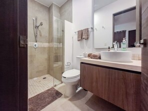 A modern bathroom with a glass-enclosed shower, a toilet, a sink with a mirror above, and a wooden cabinet. - Modern Apt Tulum with 2 BDR Gym & Pool (Tulum)