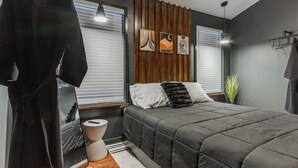 A modern bedroom with a bed, bedside tables, a hanging robe, and artwork on the wall. - The Iverson - Urban Core OKC (Oklahoma City)