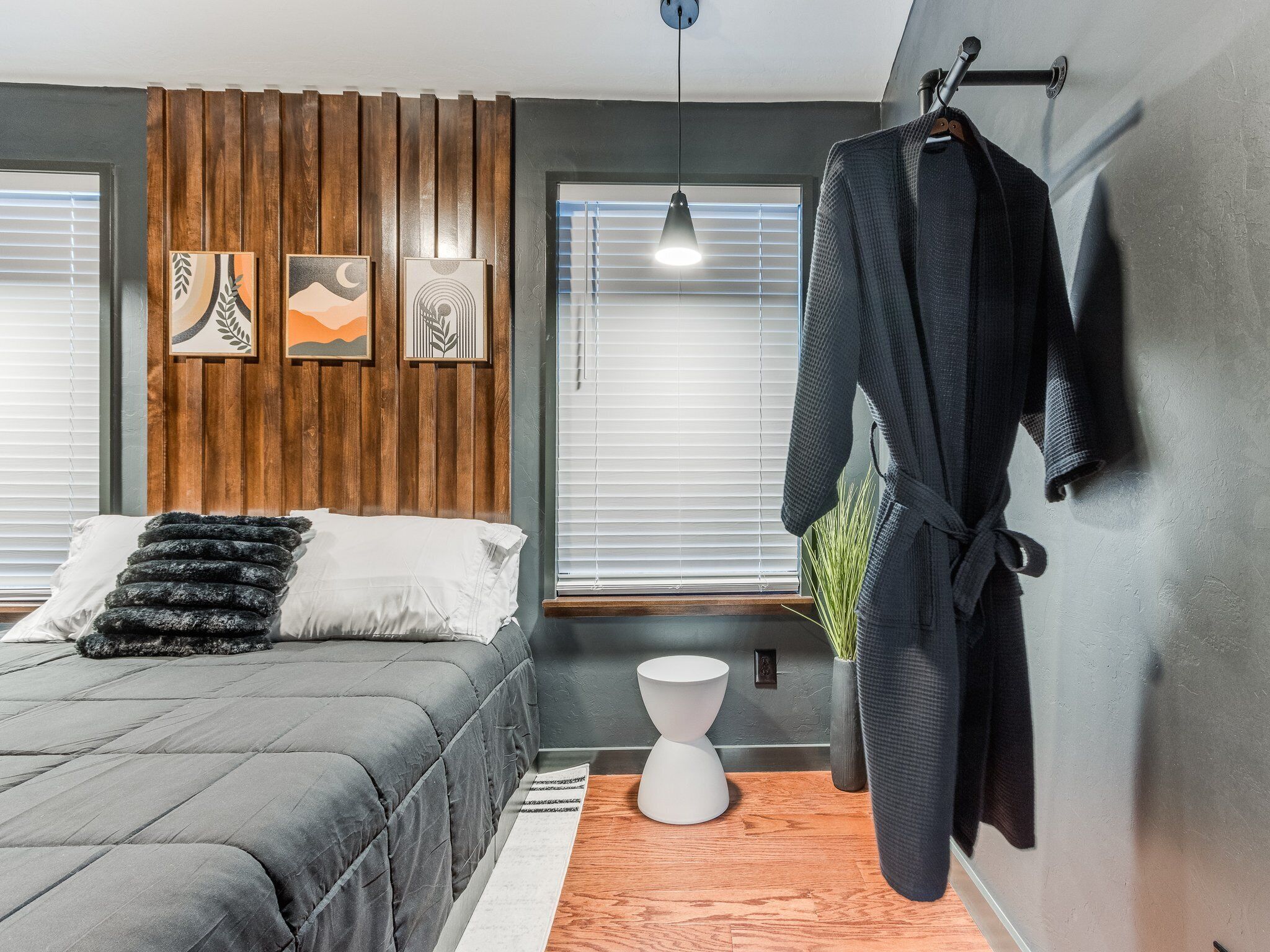 Une chambre à coucher moderne, comprenant un lit, une table de chevet, un porte-manteau mural et des œuvres d’art.