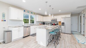 A modern kitchen with white cabinets, a central island with bar stools, stainless steel appliances, and pendant lighting. - New! Lake, Dock, Pool Table, Firepit, Deck, Yard, Firepit (Henrico)