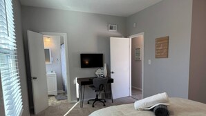 Een slaapkamer met een bed, een bureau, een stoel, een televisie en een deur naar een andere kamer.