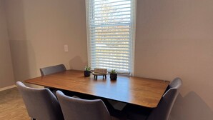 Een eetkamer met een houten tafel, vier grijze stoelen en twee potplanten.