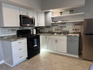 Una cucina moderna con mobili bianchi, un fornello nero, un frigorifero in acciaio inossidabile e un forno a microonde.