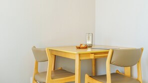 Une petite table carrée en bois, accompagnée de deux chaises, d’un porte-bougie en verre et d’un bol rempli de collations.
