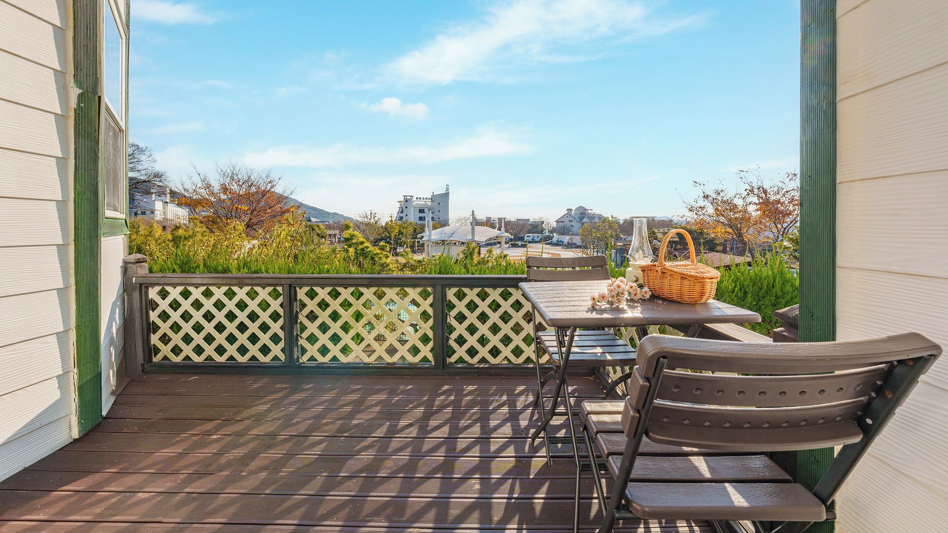 A balcony with a table and chairs, a wicker basket, and a view of buildings and trees.