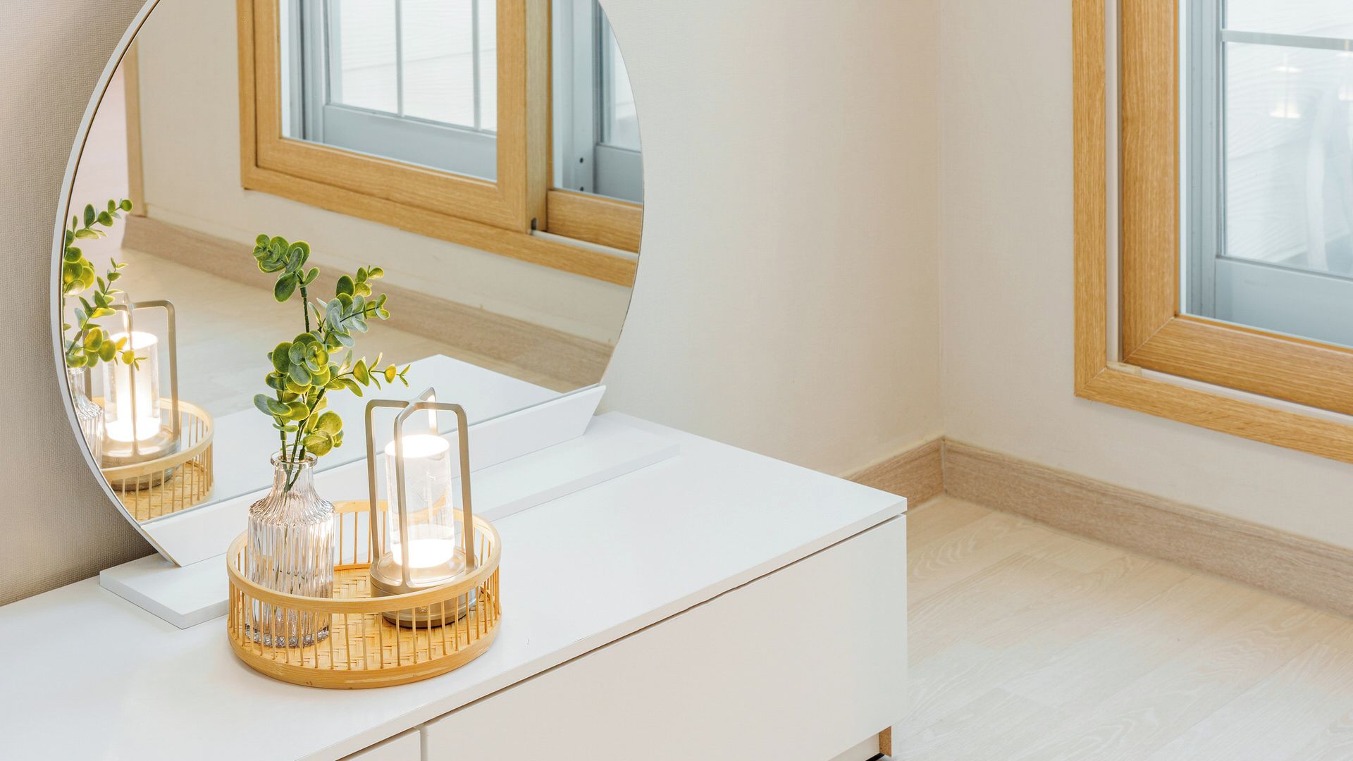 A white vanity with a mirror, a vase with green foliage, and two lit candles on a wooden tray.