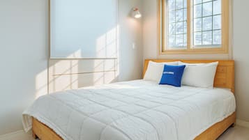 Ein Schlafzimmer mit einem Holzbett, weißer Bettwäsche, einem blauen Kopfkissen und einem Fenster mit Blick auf Bäume.