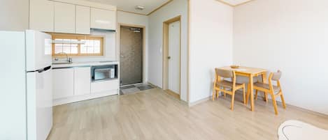 Een compacte keuken met een magnetron, koelkast en een klein eetgedeelte met een tafel en stoelen.