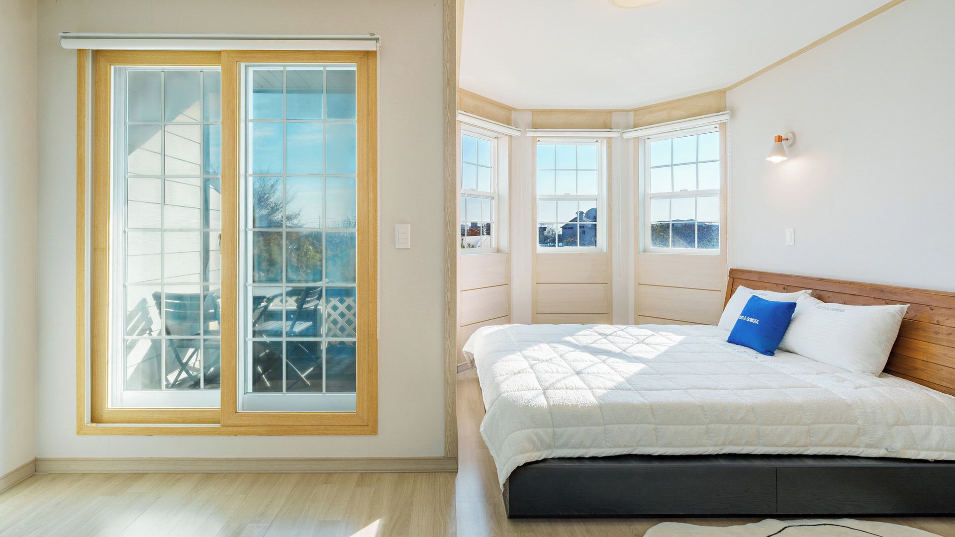 Un dormitorio con un amplio ventanal corredera, una cama con colcha blanca y vistas al exterior.