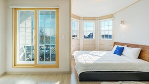 Une chambre dotée d’une grande porte-fenêtre coulissante, d’un lit recouvert d’une couette blanche et offrant une vue sur l’extérieur.