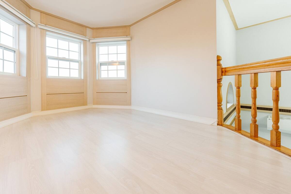 Een hoekkamer met drie grote ramen, houten vloeren en een houten trap met een glazen balustrade.